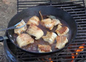 Walleye fillets frying in a cast-iron pan over a fire